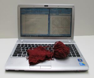 A laptop where a knitting pattern is visible on the screen, and a swatch sitting on the keyboard.